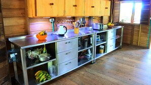 A kitchen with wooden cabinets, stainless steel countertops, and a variety of kitchen appliances and utensils. - Cabaña Kirita (Bahia Solano)