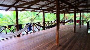 A wooden deck with a hammock and a view of palm trees. - Cabaña Kirita (Bahia Solano)