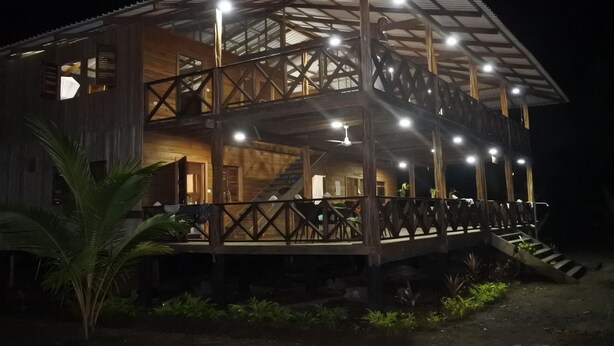 A two-story wooden building with a balcony and stairs, illuminated by multiple lights. - Cabaña Kirita (Bahia Solano)