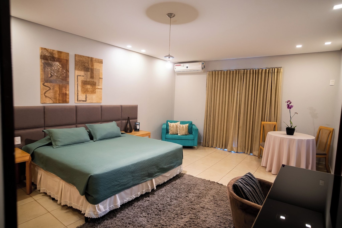 A modern bedroom with a large bed, a small sofa, a round table, and a potted plant.