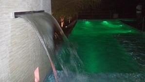 A nighttime view of a pool with a waterfall feature and green lighting. - Hotel das Palmeiras (Paracatu)