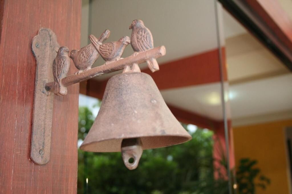 A rustic bell with two wooden birds perched on a branch, attached to a wooden structure.
