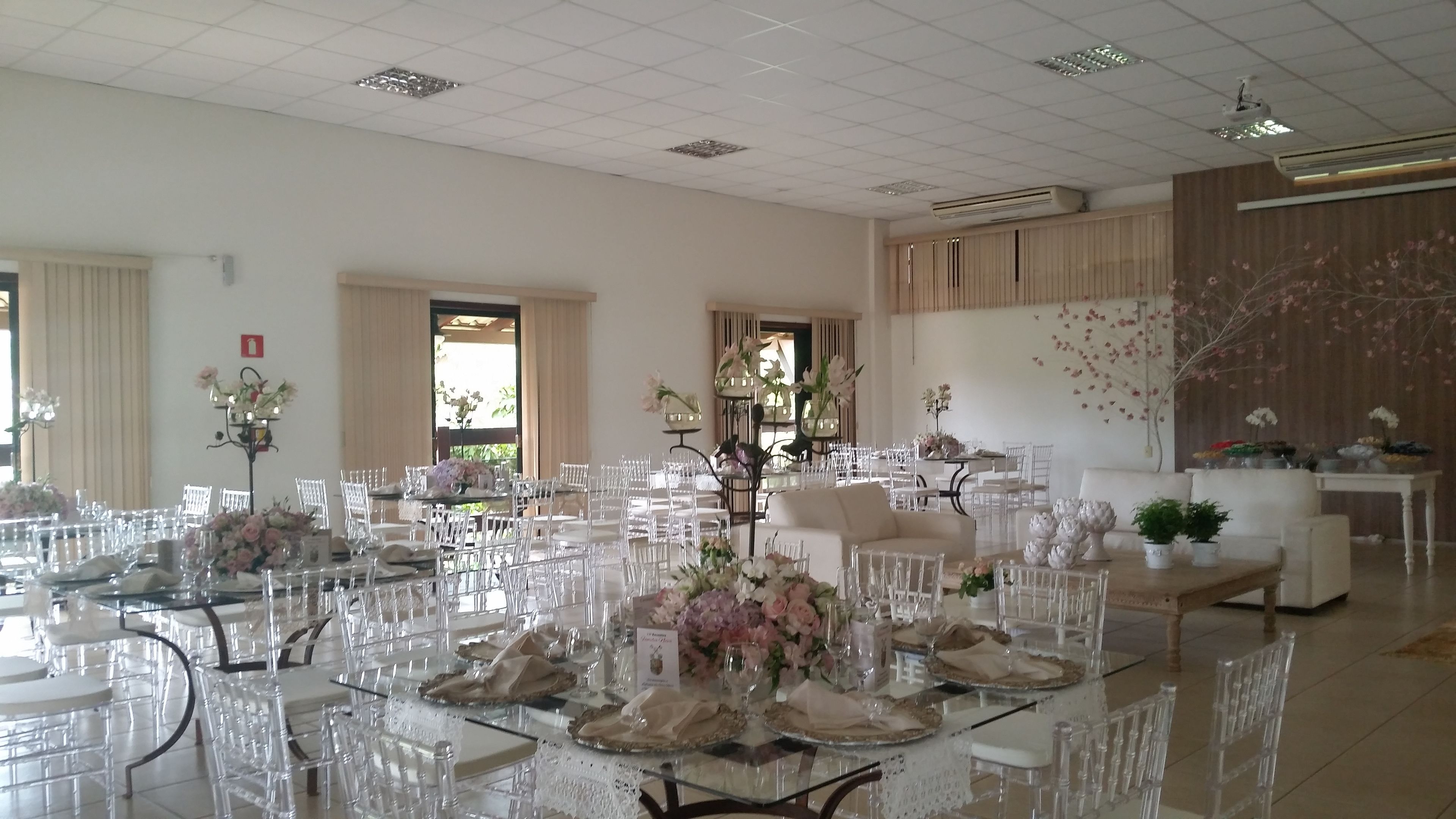 A spacious room with multiple tables set for dining, clear glass chairs, and floral centerpieces.