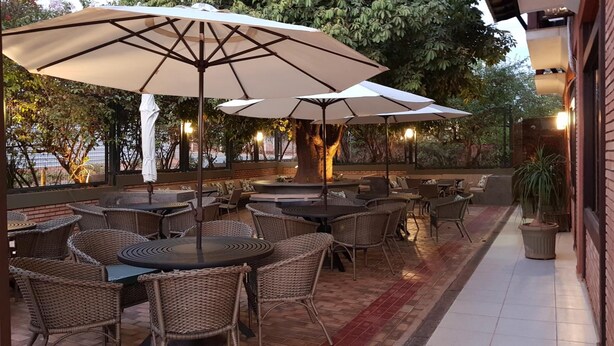An outdoor patio with wicker tables and chairs, large umbrellas, and a brick wall. - Hotel das Palmeiras (Paracatu)