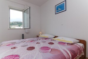 Ein Schlafzimmer mit einem Bett, einem Fenster, einer Nachttischlampe und einem gerahmten Bild an der Wand.