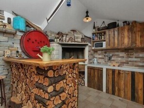 Una cocina con pared de piedra, armarios de madera, horno empotrado y un centro de mesa con un tronco de madera.