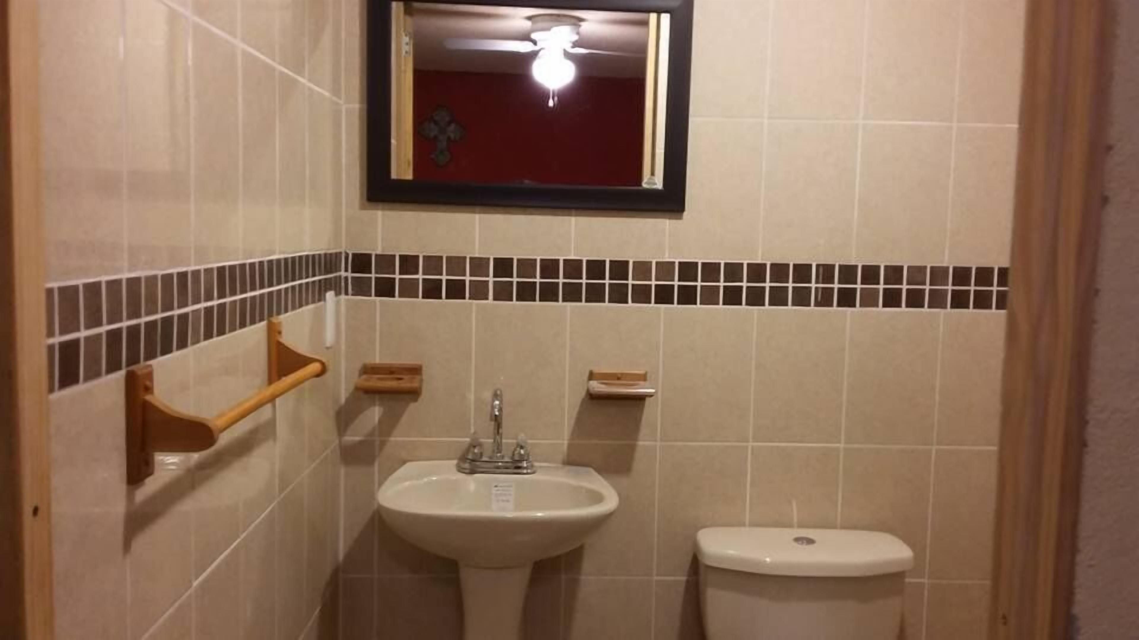 Et lille badeværelse med håndvask, toilet og et spejl over vasken.