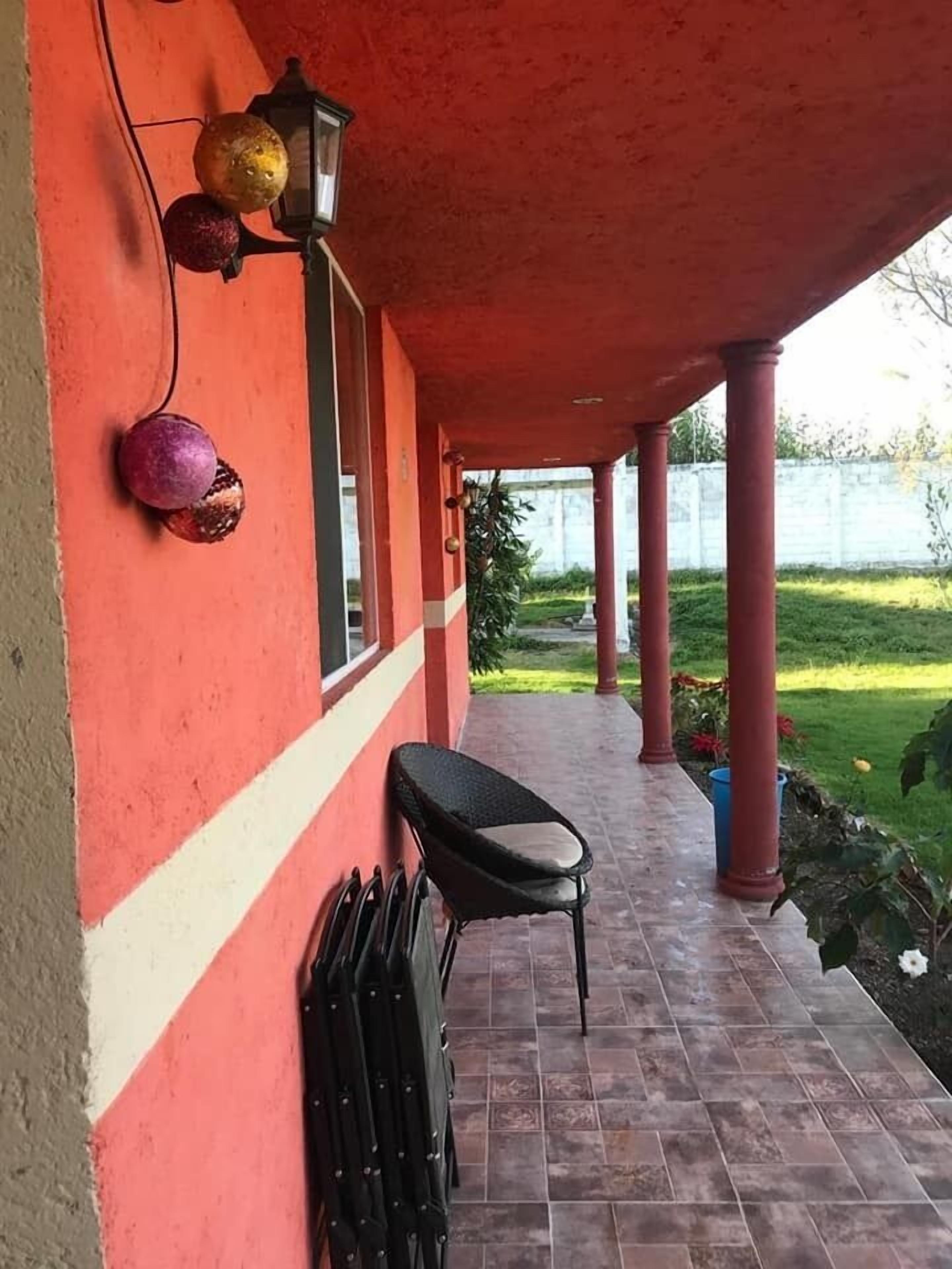 A covered outdoor area with a red wall, a black chair, and a lamp.