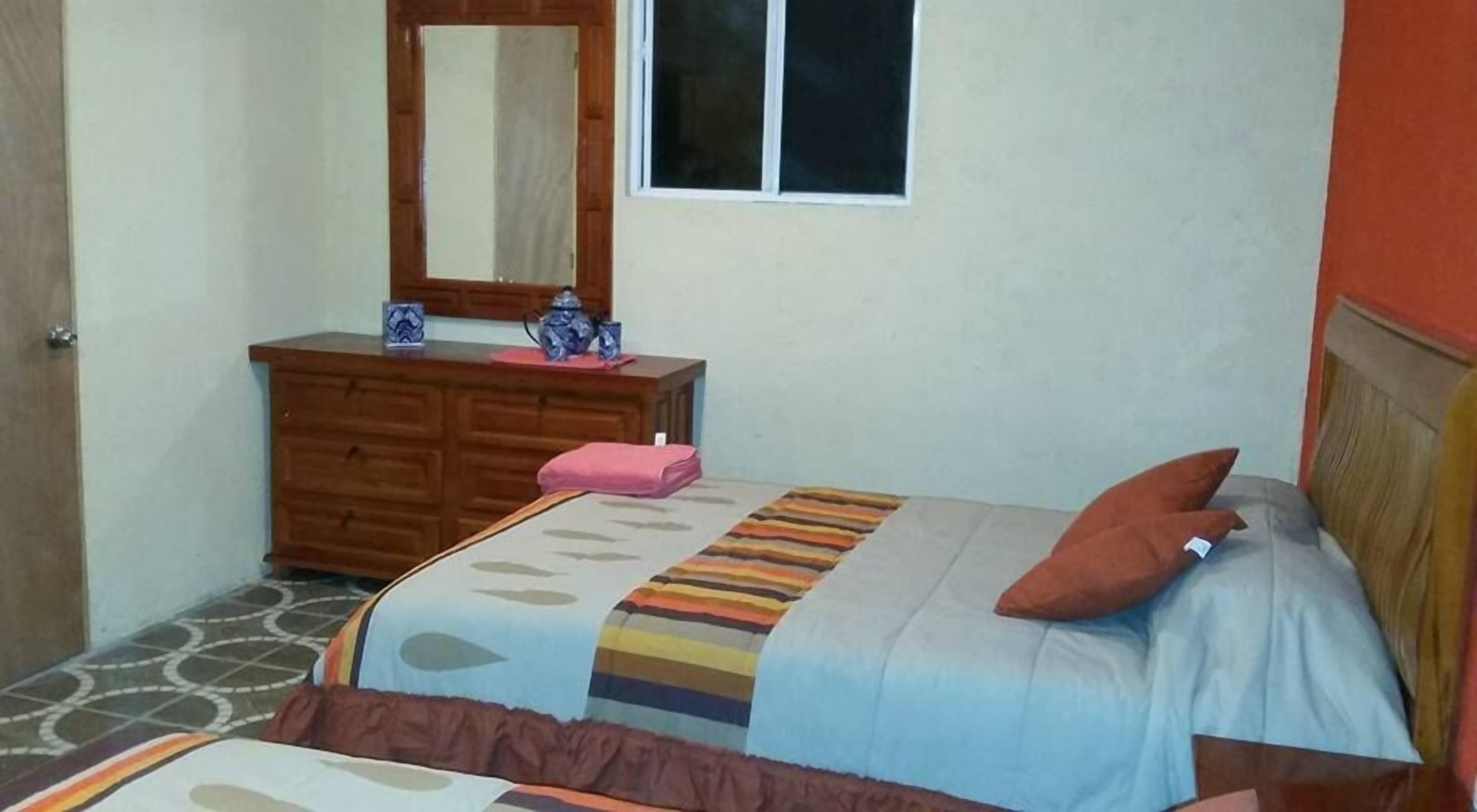 A bedroom with two beds, a dresser, a mirror, and a window.