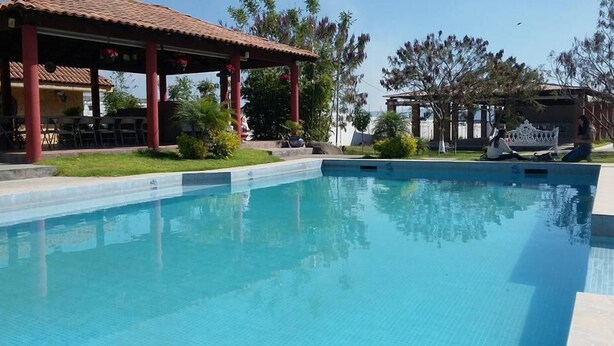 Une piscine dotée d’une terrasse carrelée, entourée de verdure et agrémentée d’un espace salon abrité.