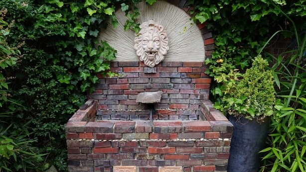 A brick structure with a lion head sculpture, surrounded by greenery. - Apartment 1 - Apartments Tovar (Wittmund)