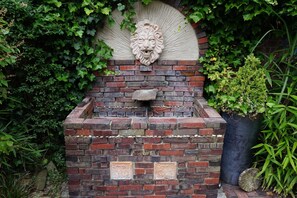 A brick structure with a lion head sculpture, surrounded by greenery.