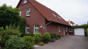 A red brick house with a sloped roof, a garage, and a well-maintained garden. - Apartment 1 - Apartments Tovar (Wittmund)