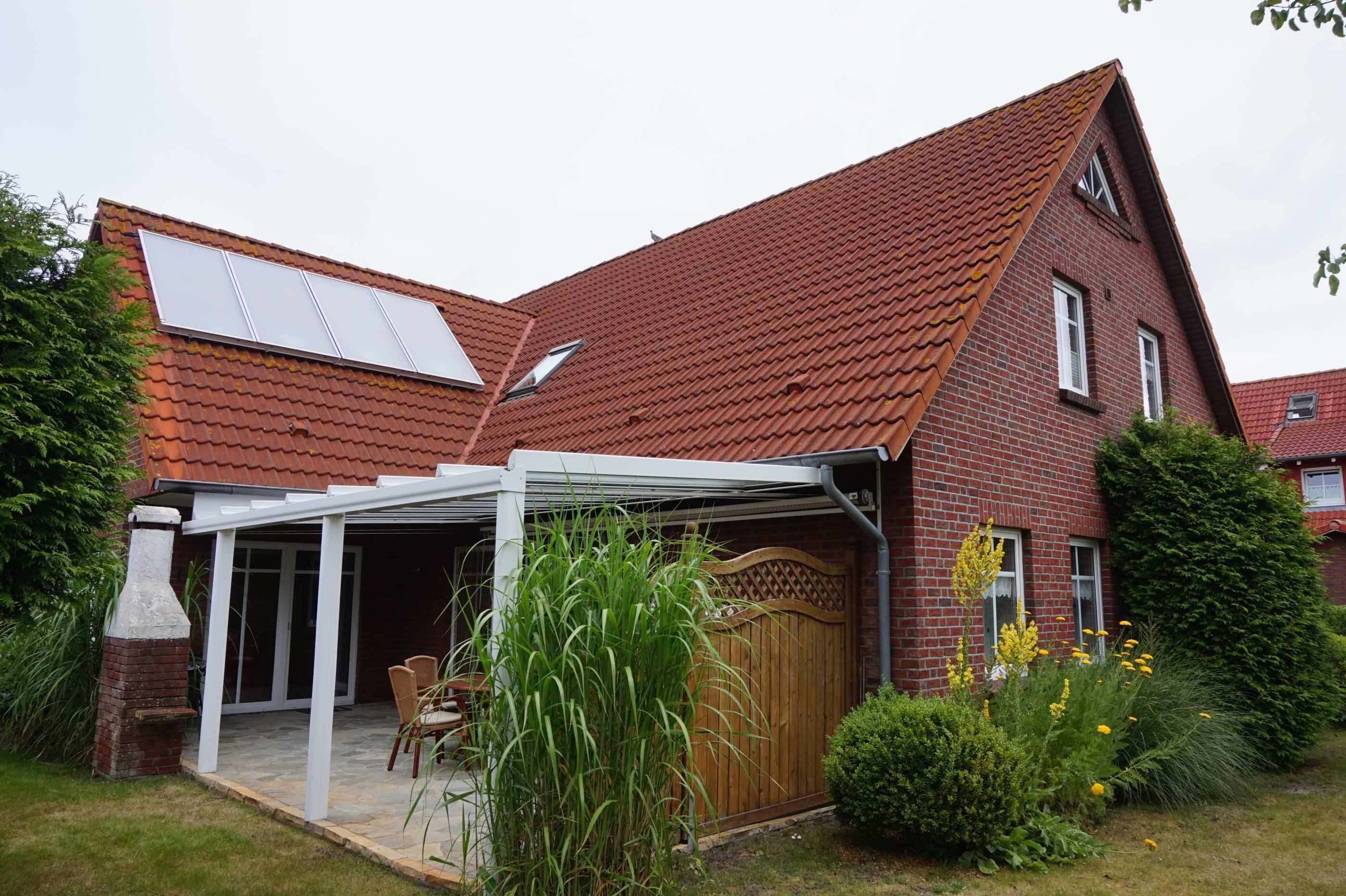 A house with a sloped red-tiled roof, a brick exterior, and a covered patio area with a table and chairs.