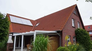 A house with a sloped red-tiled roof, a brick exterior, and a covered patio area with a table and chairs. - Apartment 1 - Apartments Tovar (Wittmund)