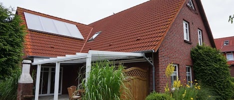 A house with a sloped red-tiled roof, a brick exterior, and a covered patio area with a table and chairs.