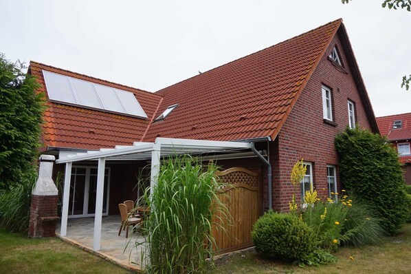 A house with a sloped red-tiled roof, a brick exterior, and a covered patio area with a table and chairs.