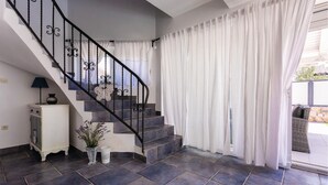 A staircase with black railings and white curtains, leading to a balcony with a wicker chair and a potted plant. - Luxurious home in Kornic (Kornic)