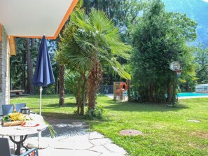 A patio area with a table set for dining, surrounded by lush greenery and a basketball hoop. - Poolside by Interhome (Castro)