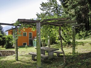 A garden with a wooden pergola, a stone bench, and a small building with a green door. - Poolside by Interhome (Castro)