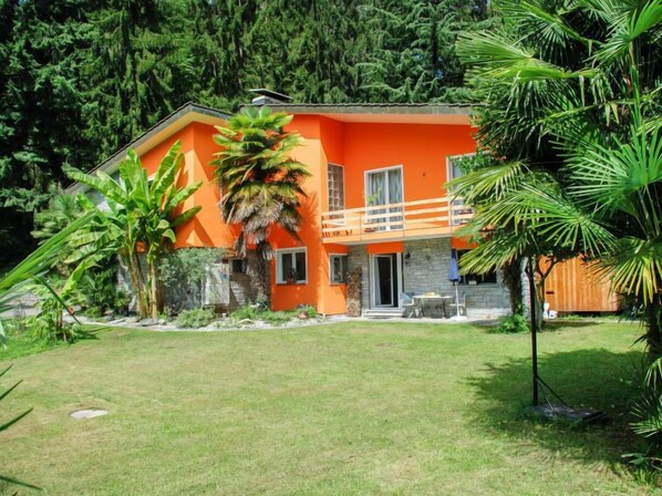 A two-story house with an orange exterior, surrounded by lush greenery and a well-maintained lawn. - Poolside by Interhome (Castro)