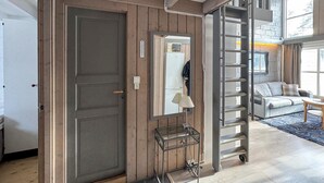 Een kamer met een houten deur, een metalen ladder, een spiegel en een bank.