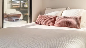 Una cama bien hecha con un edredón blanco texturizado y dos almohadas rosas.