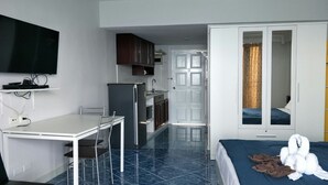 Quarto de hotel com cama, escrivaninha com cadeira, televisão na parede, armário e porta para o banheiro.