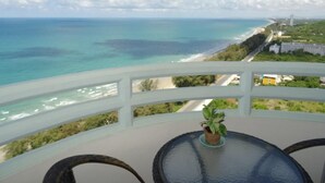 Uma varanda com vista para o oceano e a praia, uma mesa com uma planta e cadeiras de vime.