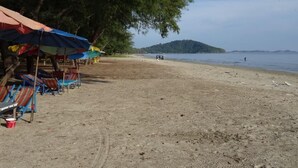 Uma praia com guarda-sóis e espreguiçadeiras, uma faixa de areia e uma ilha ao longe.