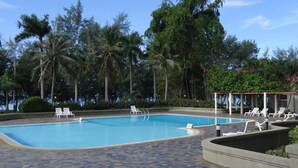 Piscina com espreguiçadeiras e palmeiras ao fundo.