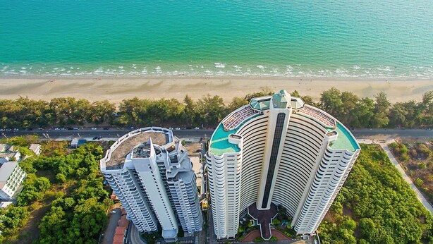 Um hotel alto com fachada curva, localizado perto de uma praia com areal e uma estrada em primeiro plano.