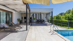 Ein moderner Poolbereich im Freien mit Liegestühlen, einem Grill und einer überdachten Sitzgruppe.