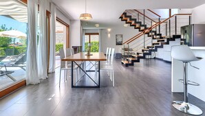 Eine moderne Küche mit eingebautem Herd, ein Essbereich mit Holztisch und -stühlen sowie eine Treppe mit Holzhandläufen.