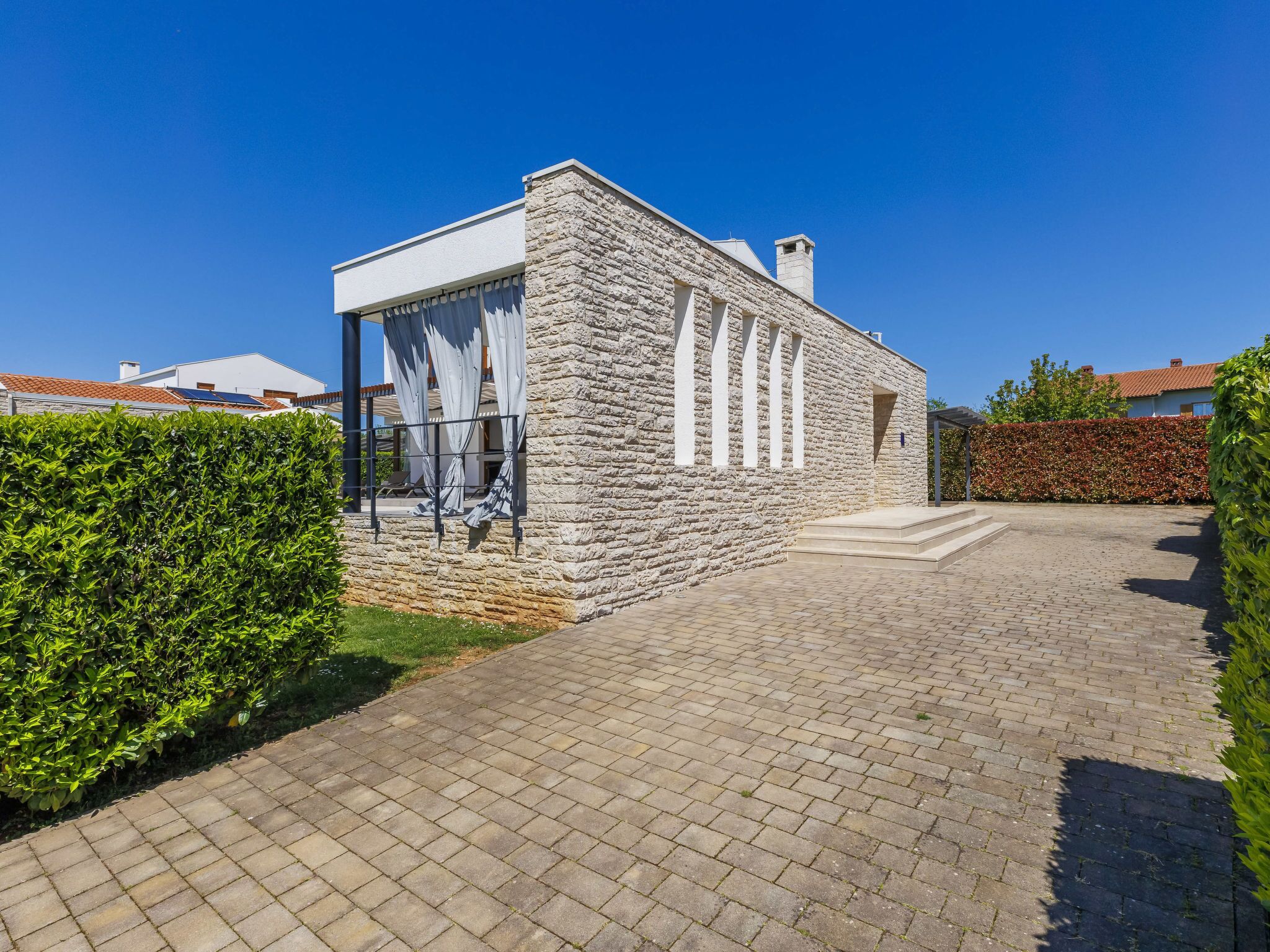 A stone building with a covered patio area, a brick pathway, and a neatly trimmed hedge.