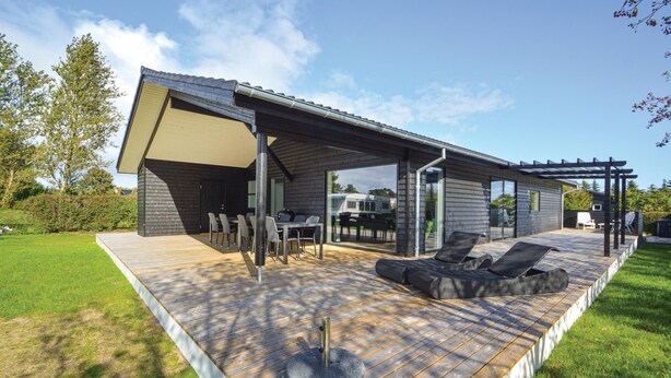Ein modernes Haus mit einer überdachten Terrasse, Sitzgelegenheiten im Freien und einem großen Fenster mit Blick auf den Garten.