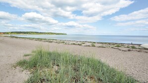 Ein Strand mit sandigem Ufer, grünen Flächen und einem ruhigen Meer unter einem teils bewölkten Himmel.