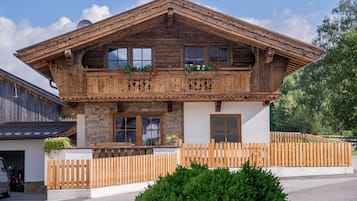 A wooden chalet with a balcony, stone facade, and a wooden fence.