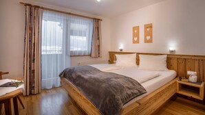 Un dormitorio con una cama de madera, una mesita de noche, una silla y una ventana con cortinas traslúcidas.