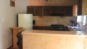 Una cocina con refrigerador, estufa, lavamanos y armarios de madera.