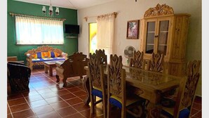 A dining area with a wooden table and chairs, a green sofa, and a cabinet with glass doors. - Quinta Comala (Comala)