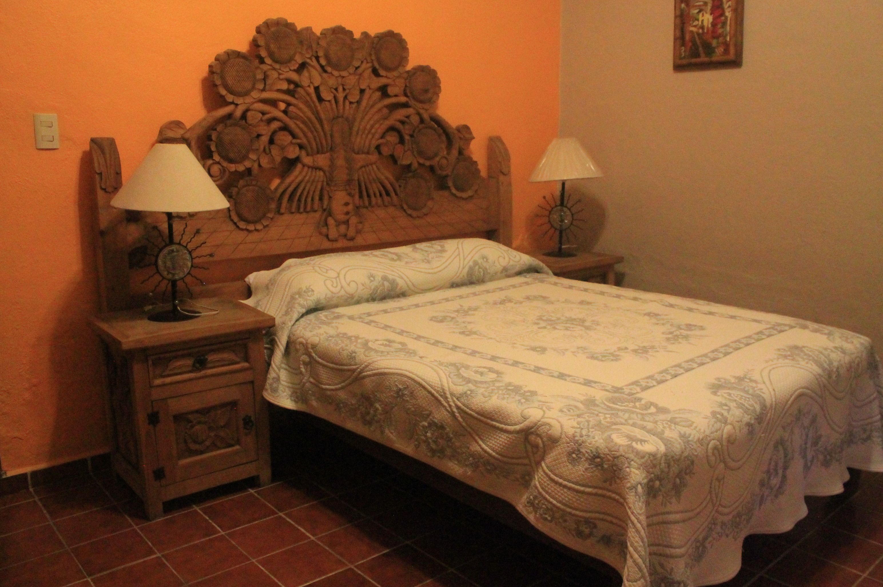 Una cama con cabecera floral, dos lámparas de noche y un adorno en la pared.