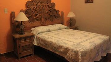 Una cama con cabecera floral, dos lámparas de noche y un adorno en la pared.