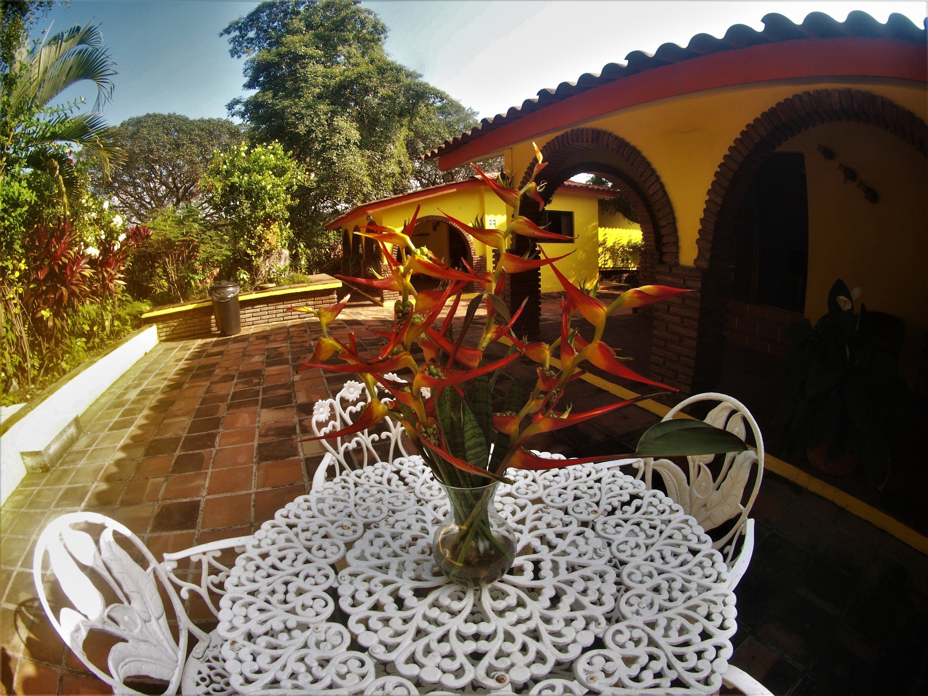 A white intricately designed table with a clear glass vase containing red and yellow flowers.