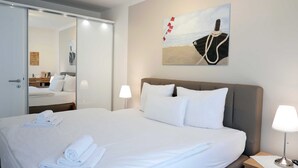 A hotel room with a large bed, a painting of a boat on the wall, a bedside lamp, and a mirror.
