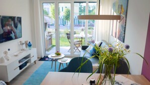A modern living room with a dining table, a vase with flowers, a sofa, and a television.