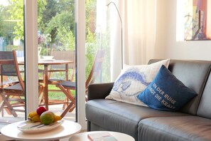 Un salon avec un canapé, une table sur laquelle se trouve un panier de fruits, et une vue sur l’extérieur.