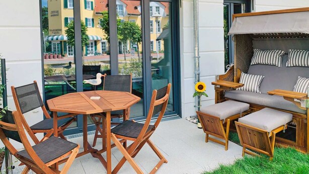 An outdoor seating area with a round wooden table, folding chairs, and a cushioned sofa with striped pillows.