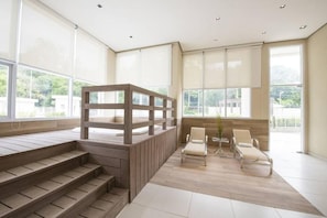 Un interior moderno con una escalera de madera, una zona de estar con dos sillones y ventanas grandes.