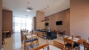 Un área de comedor moderna con mesas y sillas de madera, una barra central y un televisor de pantalla plana montado en la pared.